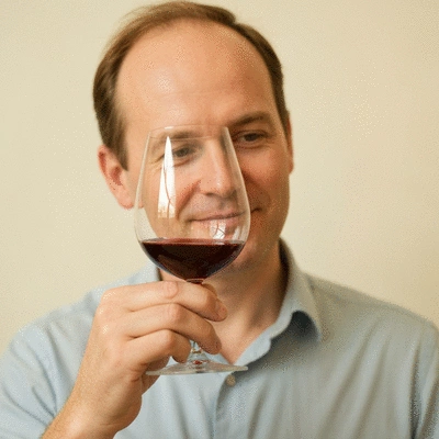 Person holding a glass of aged red wine, inspecting its color and aroma