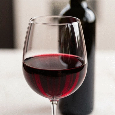 Close-up of a glass of red Shiraz wine with a bottle blurred in the background, showcasing rich color and texture